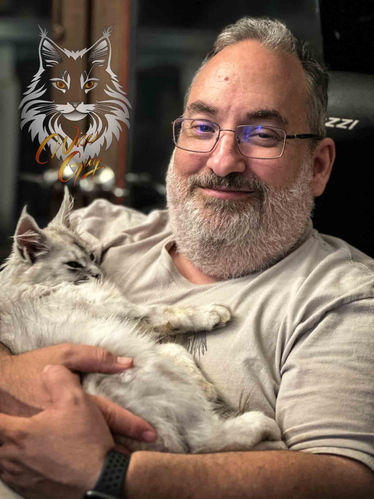 A person in a grey t-shirt, with a beard, holding a relaxed white cat, with a detailed illustration of a cat’s face floating above.
